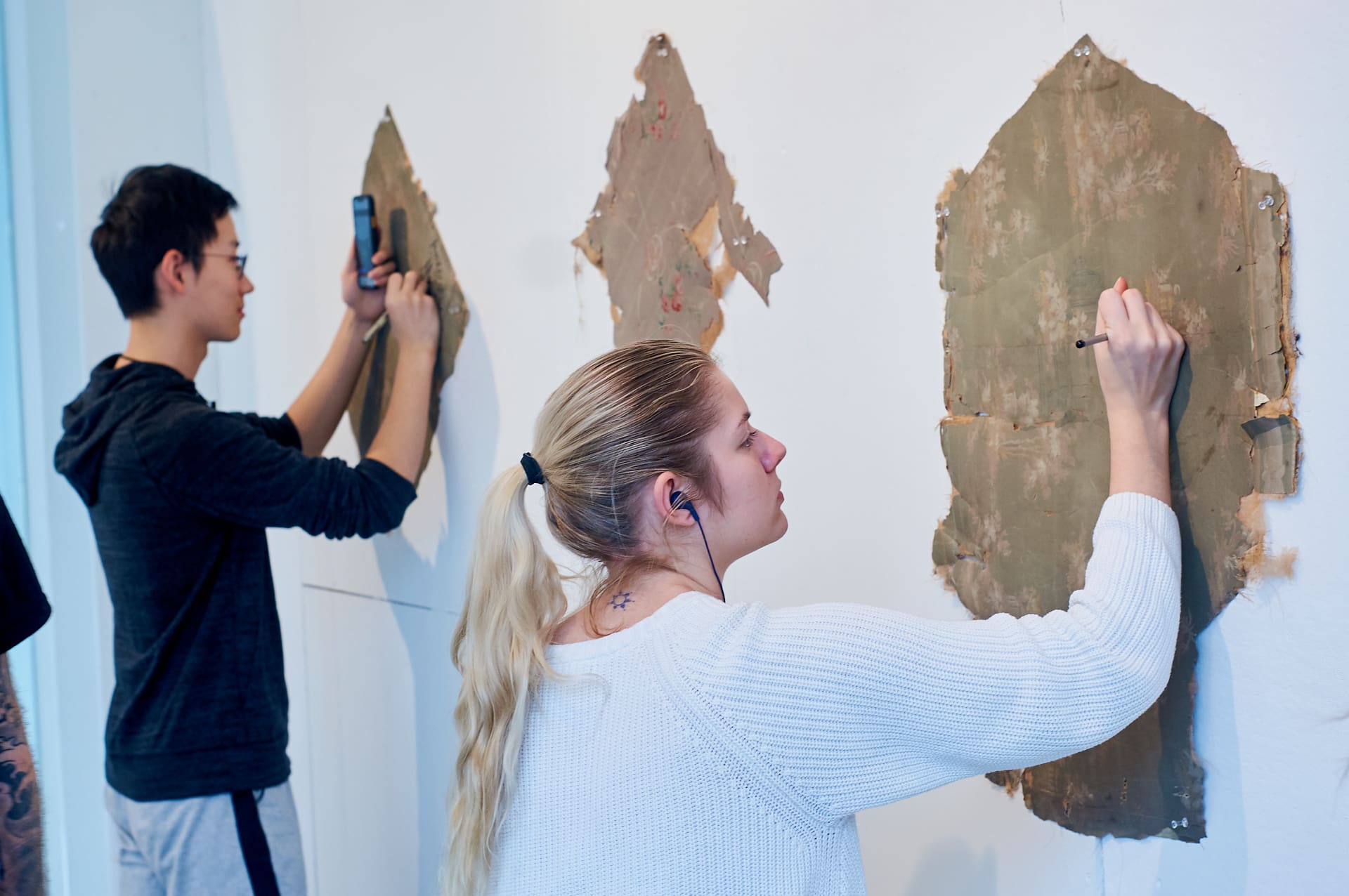 Students drawing on salvaged wallpaper tacked to a wall