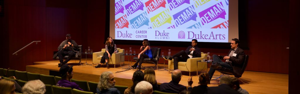 Three panelists on a stage talking to a group of audience members