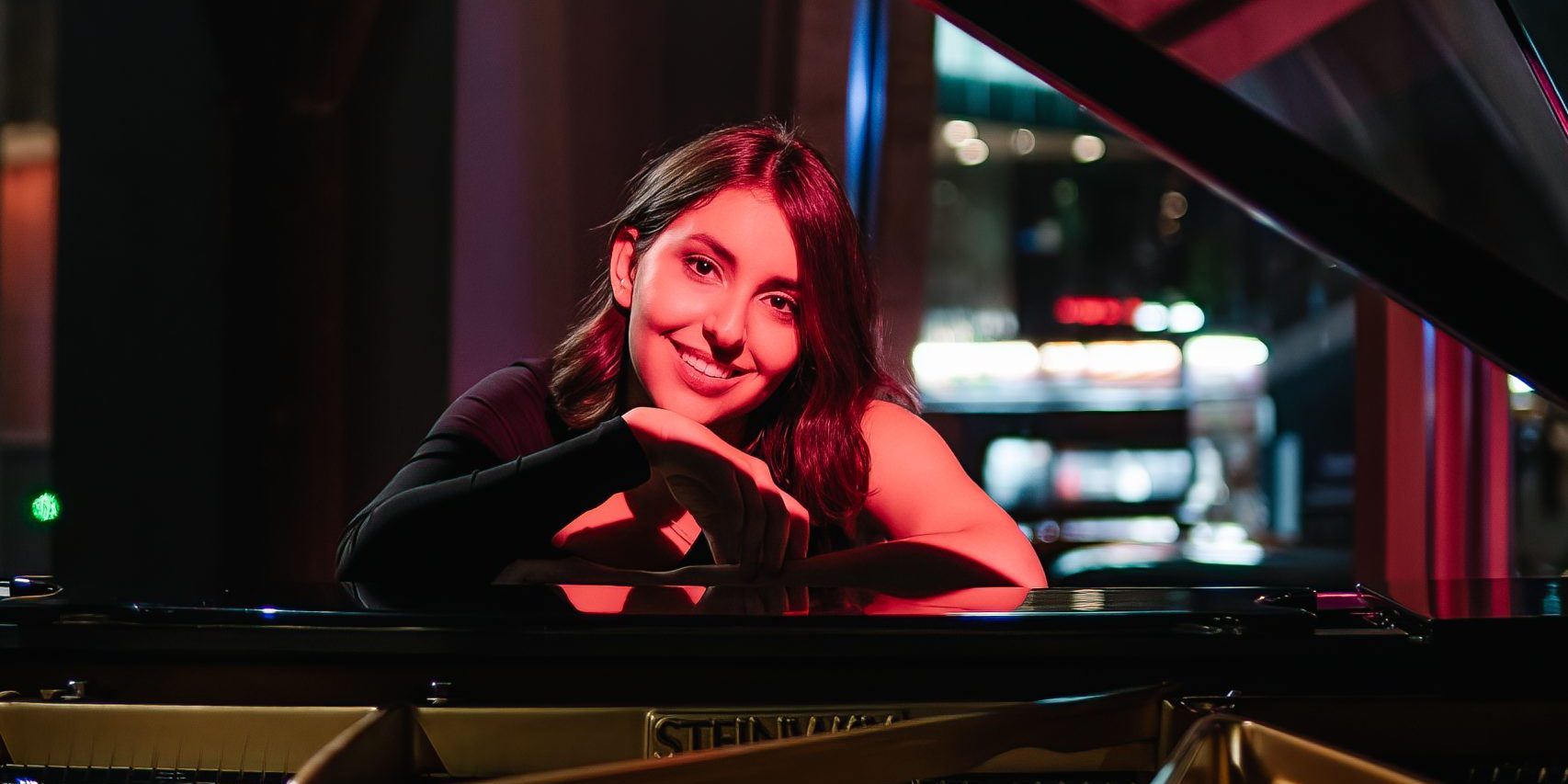 Young woman leaning on a black grand piano.