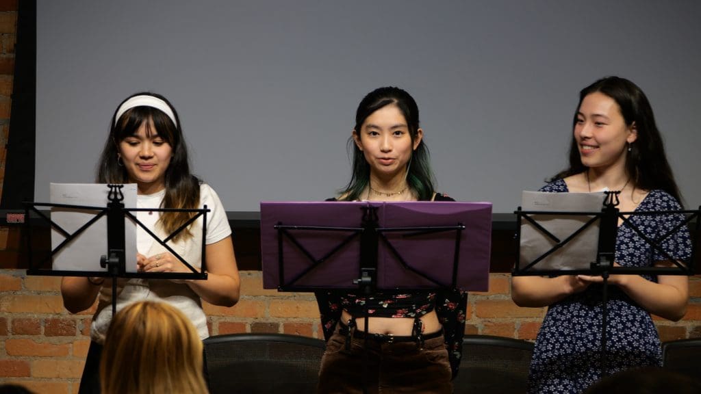 Three young adult women standing behind music stands