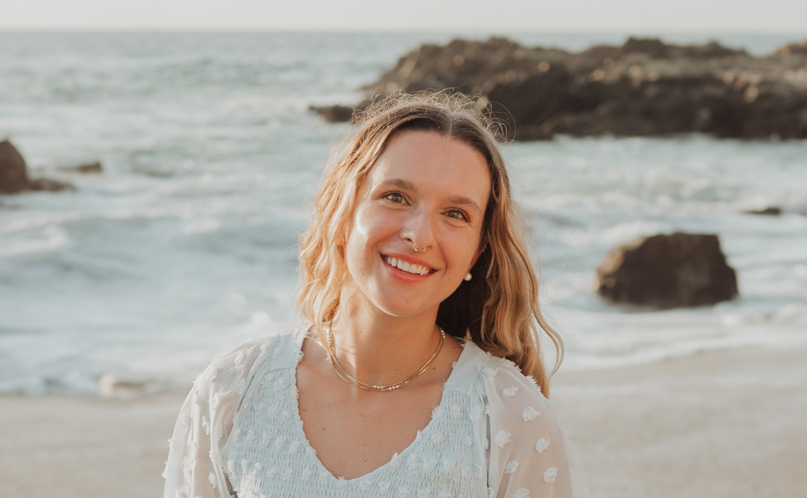 A young adult women with blonde wavy hair smiling at the beach