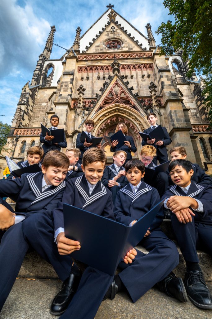 German boys in navy outfits sitting by a chapel and reading their choral scores.