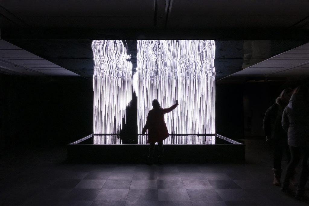 A black silhouette in front of a projected video installation of a white rippling water effect