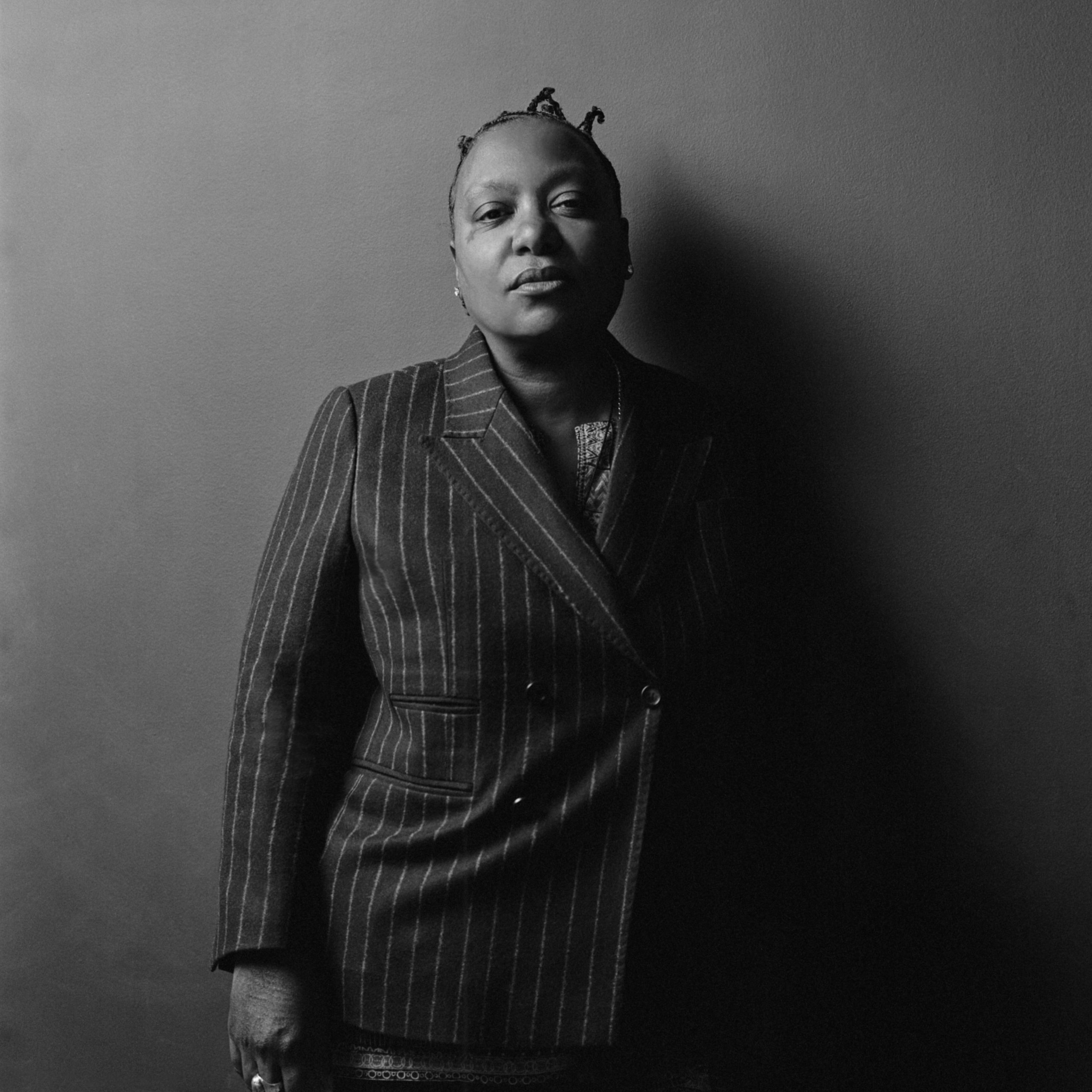 A women wearing a dark stripped suit standing with her arms down against her side