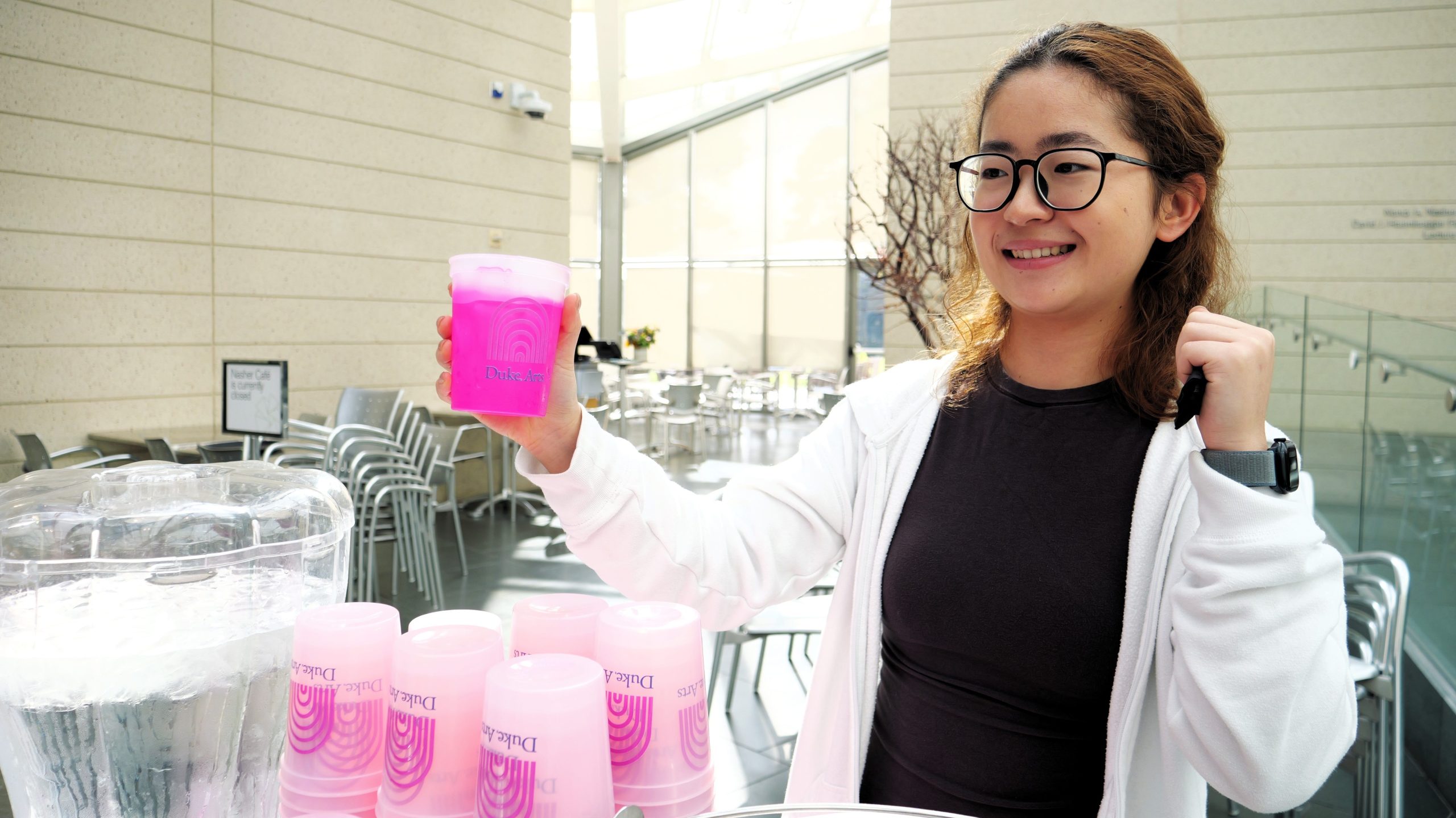 A young adult women holding up a pink reusable cup