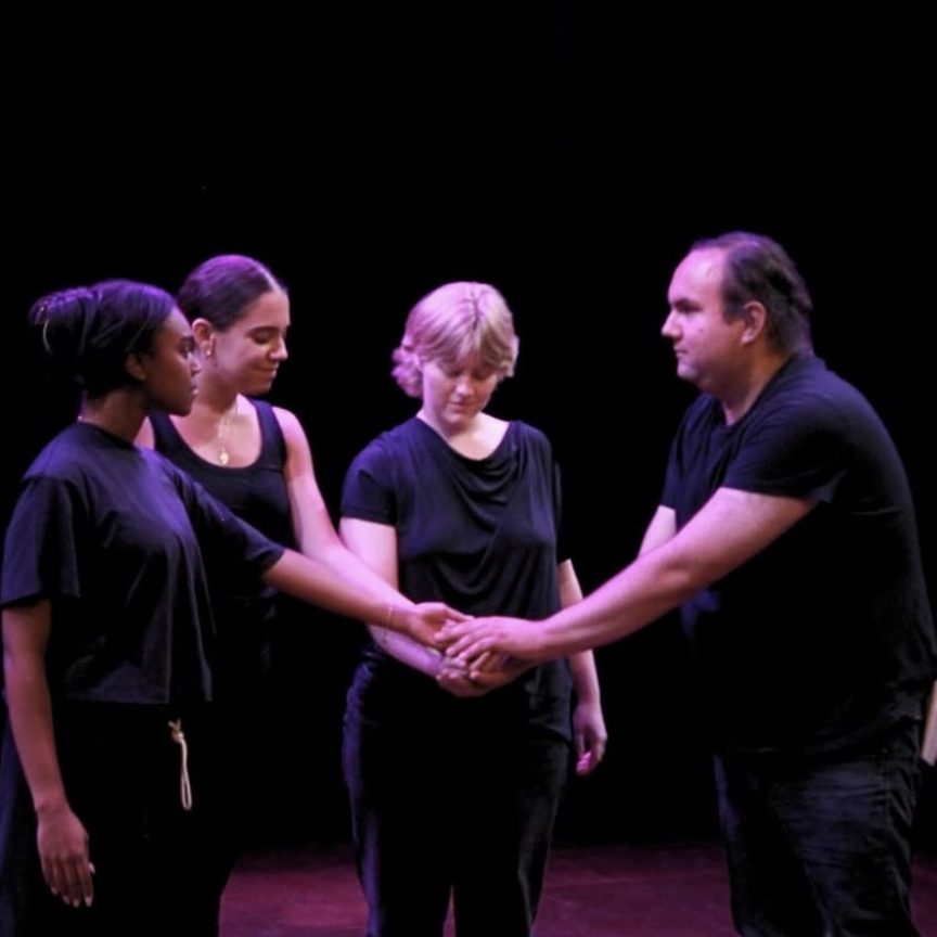 A group of four individuals gather around each other with their hands held out in the center