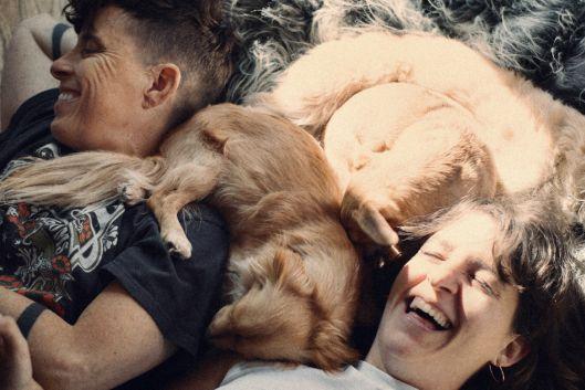 Andrea Gibson and Megan Falley lie on the floor laughing, surrounded by dogs