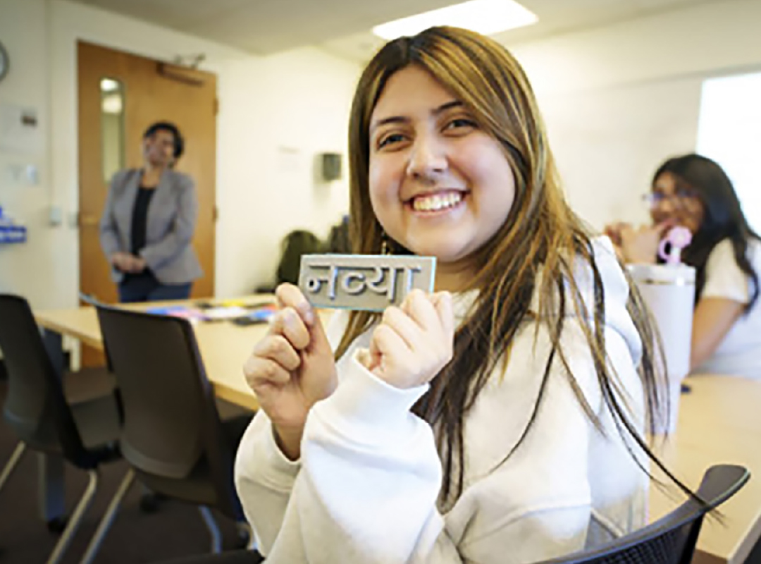 A young adult women holding a 3D-printed name in Hindi