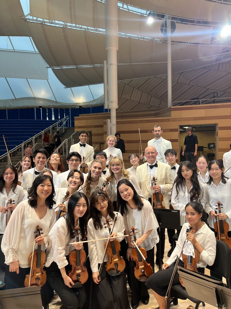 A group of young adult students smiling at the camera and posing with their chamber instruments